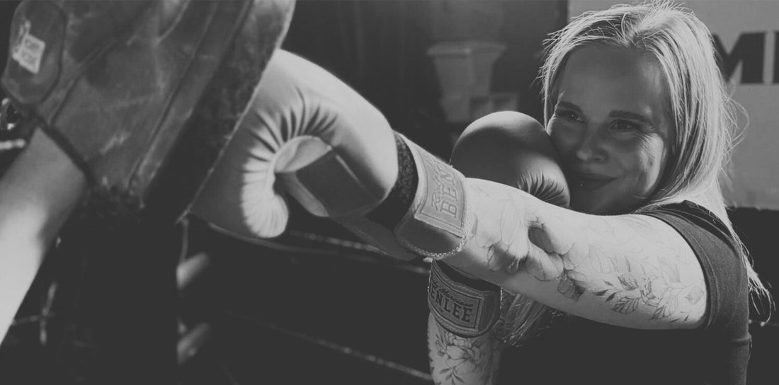 Frau mit Boxhandschuhen schlägt auf Pratze